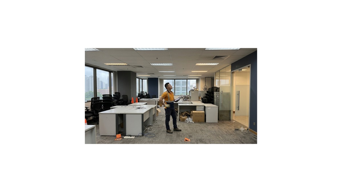 A worker in hi-vis surveying a part-cleared Singapore CBD office with disconnected desks, cabling and boxes on the floor