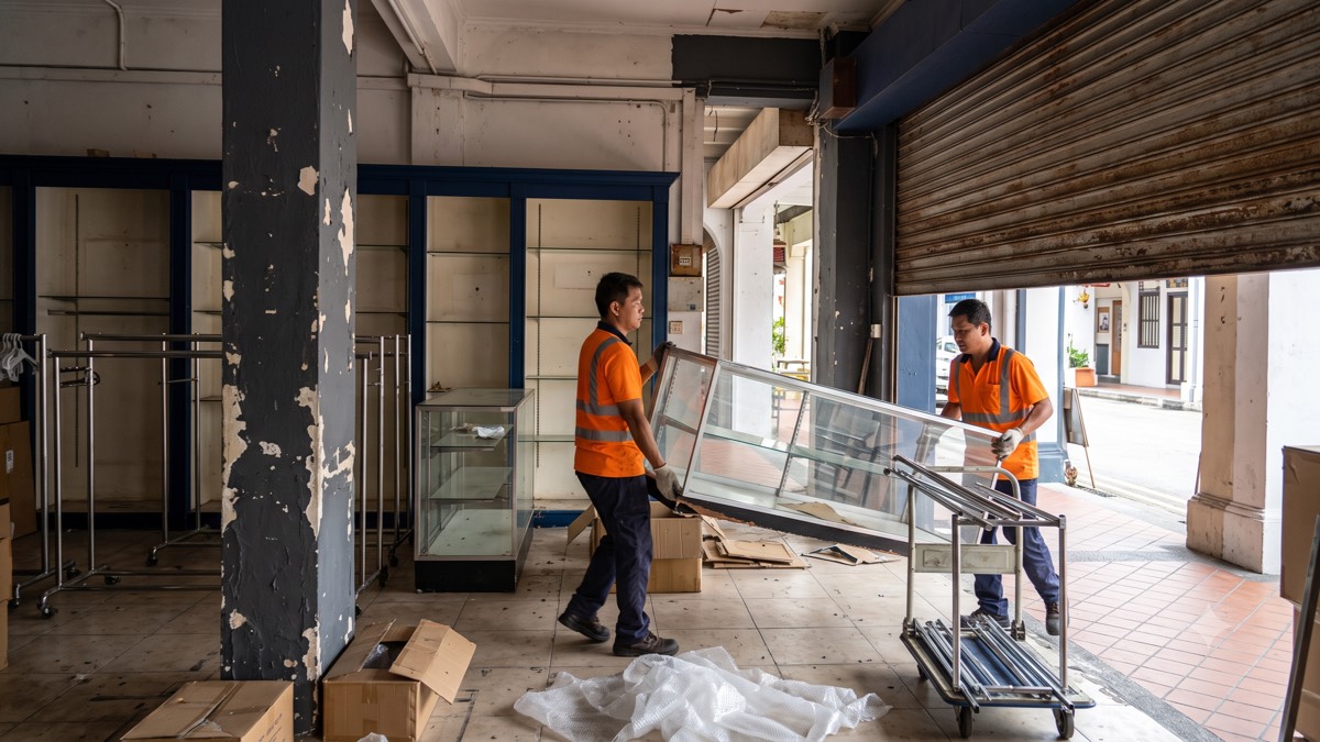 Two workers carrying a glass display counter out of a closing shophouse retail unit